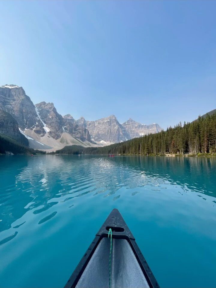 Canoe bow on turquoise lake with snow-capped mountains and pine forests in background