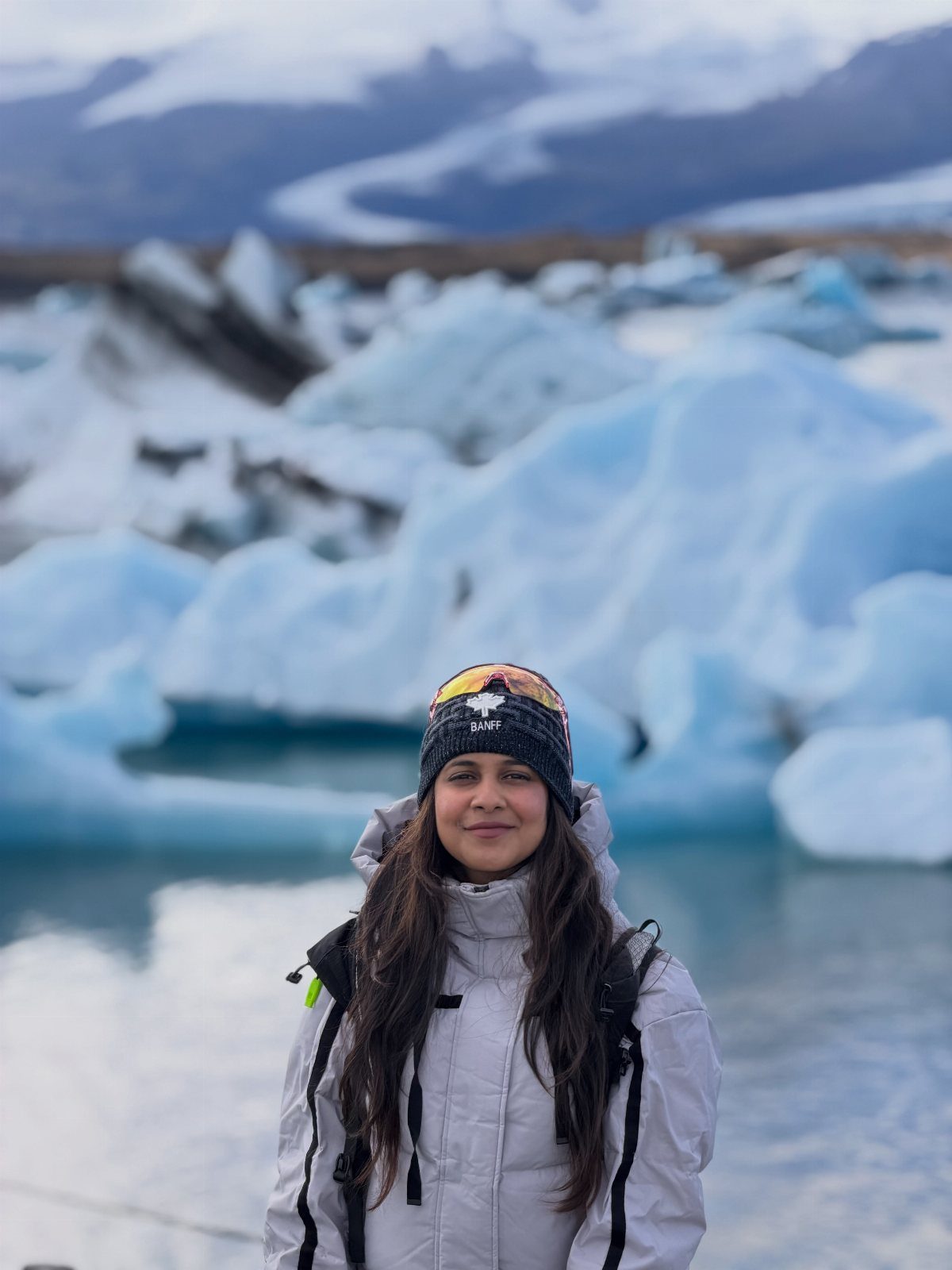 Woman in winter gear posing before blue icebergs in a glacial lagoon