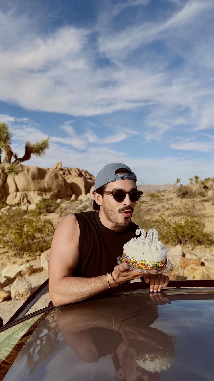 Man holding a 30th birthday cake in a Joshua Tree desert landscape.
