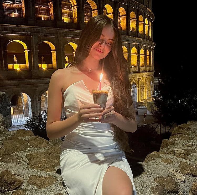Woman in white dress holding a birthday candle before the illuminated Colosseum in Rome