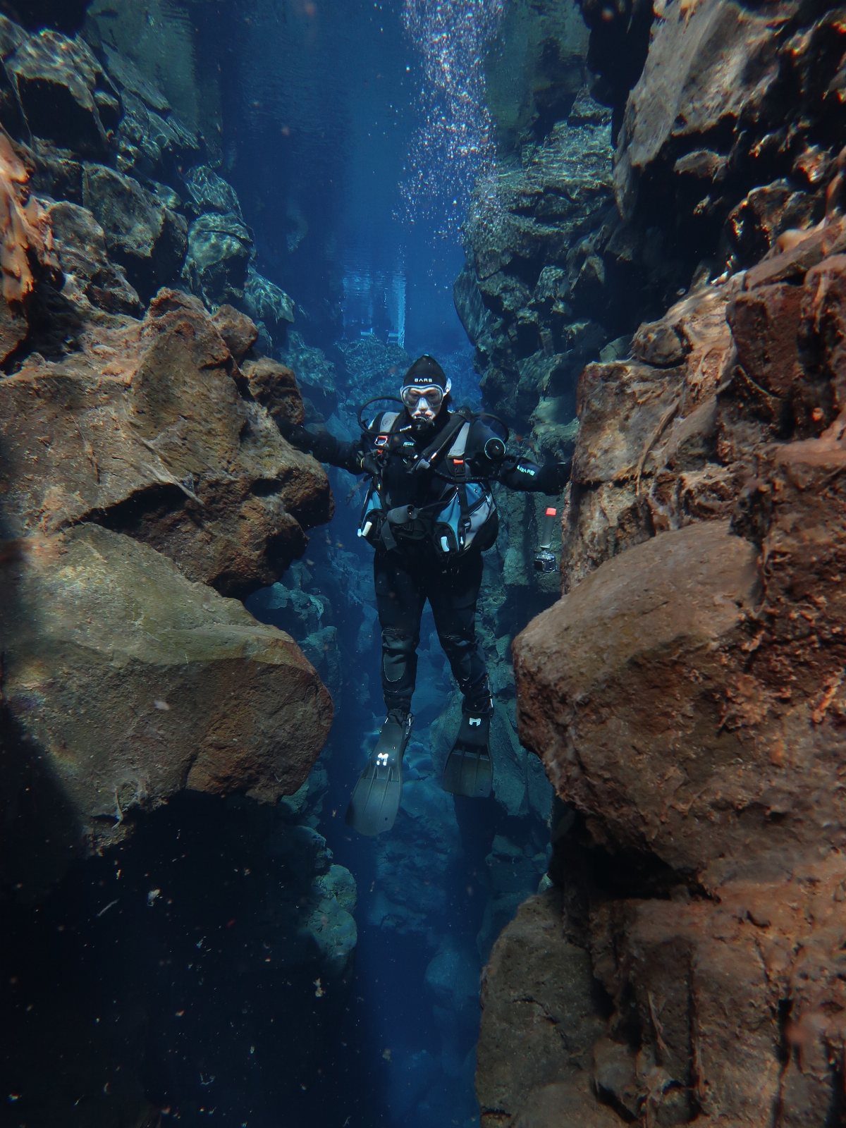 Scuba diver swimming between rocky underwater cliffs in deep blue ocean water