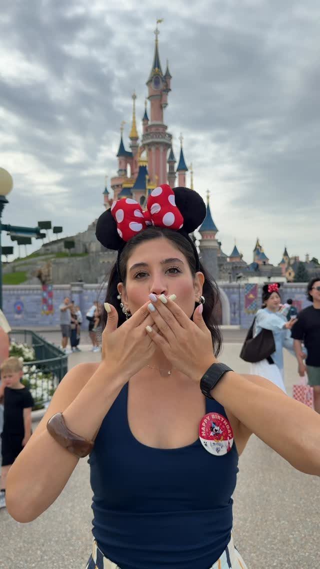 Woman wearing Mickey Mouse ears posing in front of a fairytale theme park castle