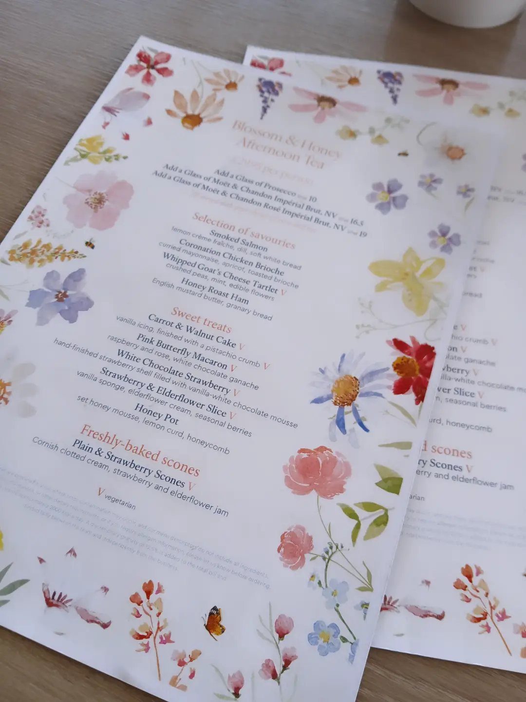 Afternoon tea menus with colorful floral watercolor borders on a wooden table