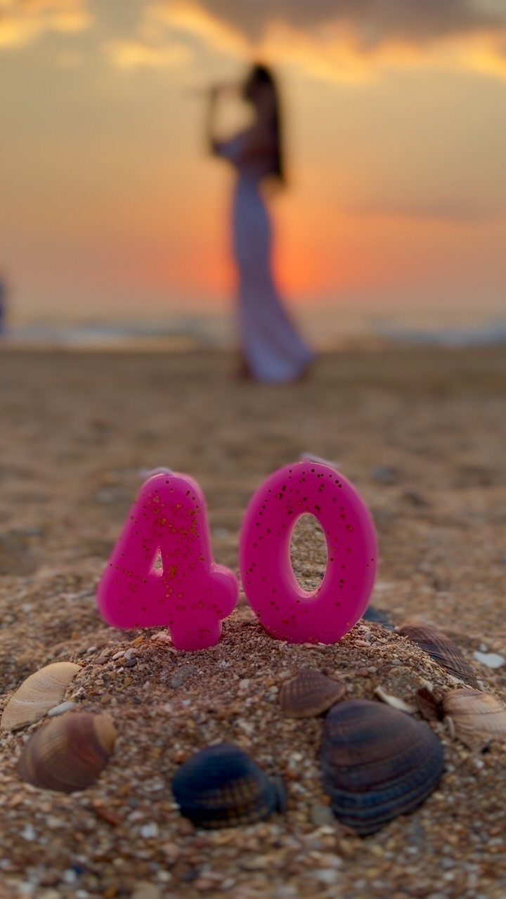 Pink number 40 candles in beach sand with seashells and a sunset background.