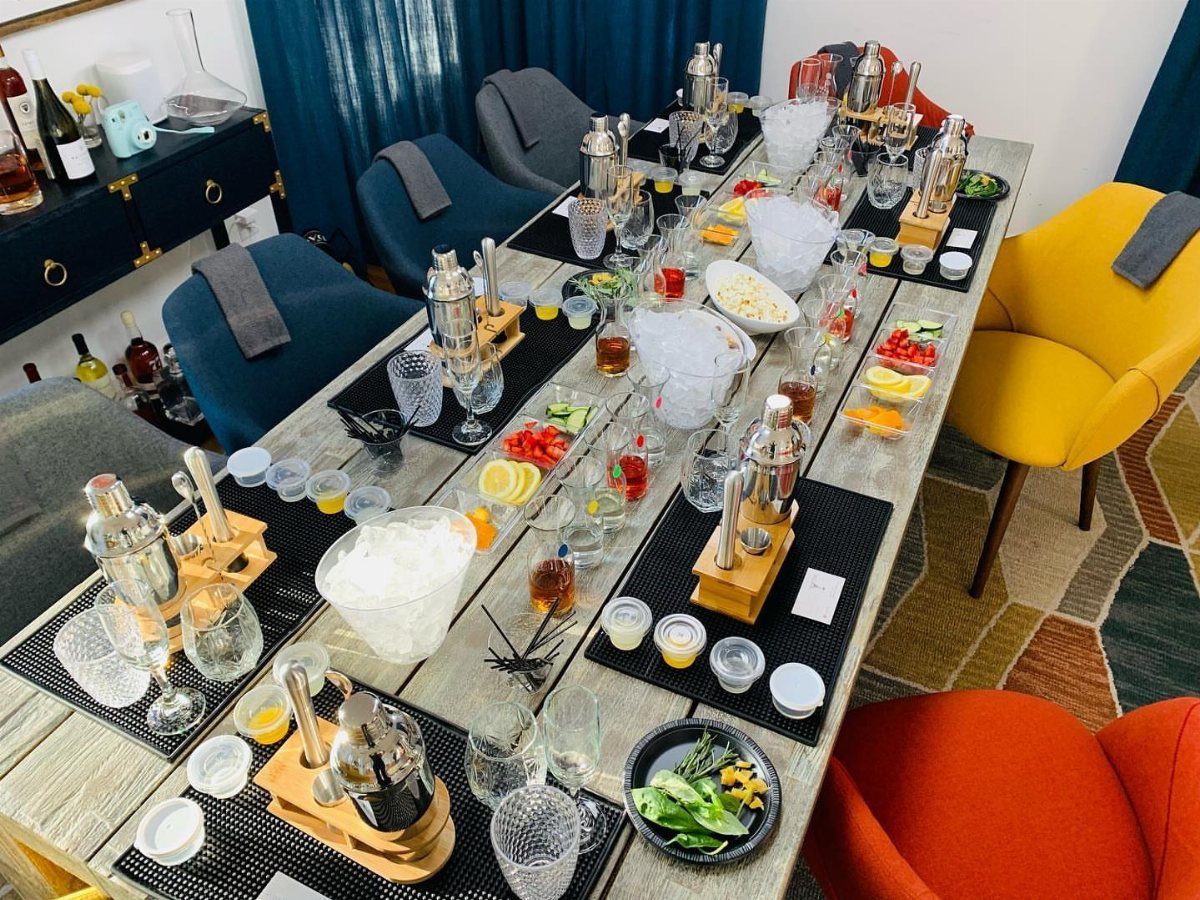 Cocktail making stations with shakers, glassware, and fruit on a long wooden table.