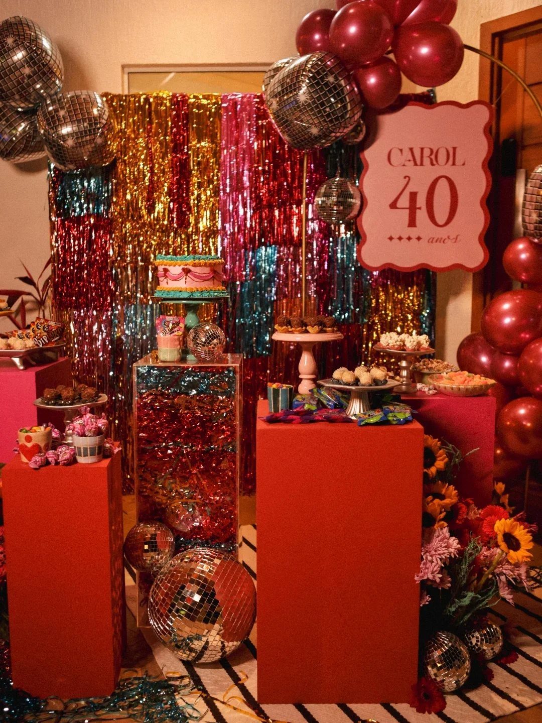 Birthday party decor with disco balls, red pedestals, and a shimmering tinsel backdrop.