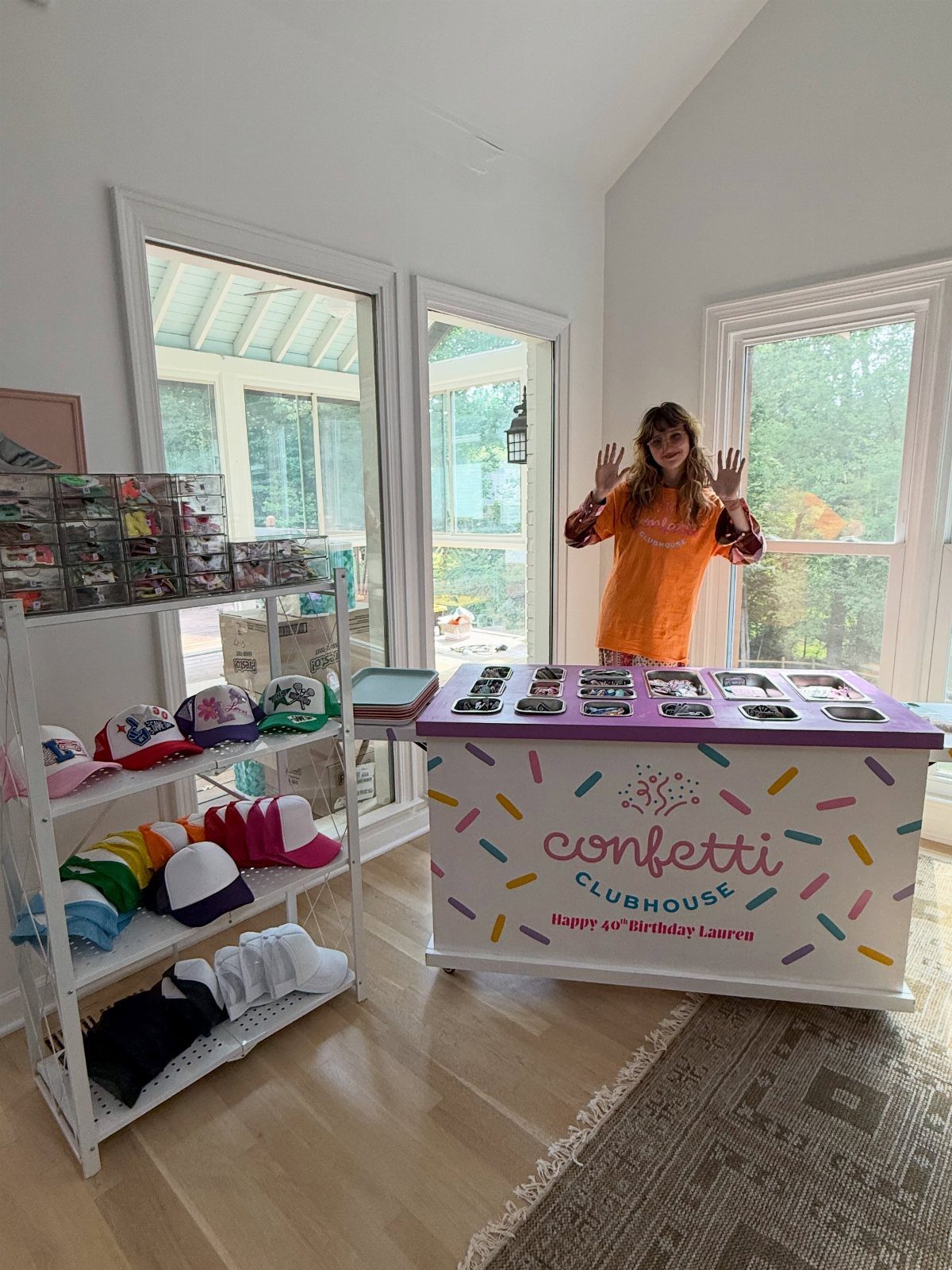 Woman standing behind a custom patch station with colorful hats on a shelf.