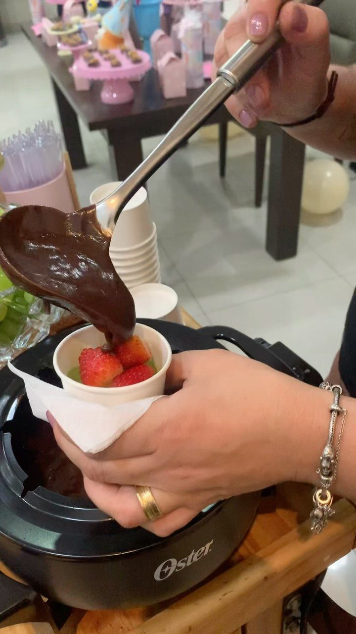 Strawberry being dipped into a chocolate fondue pot at a party setting