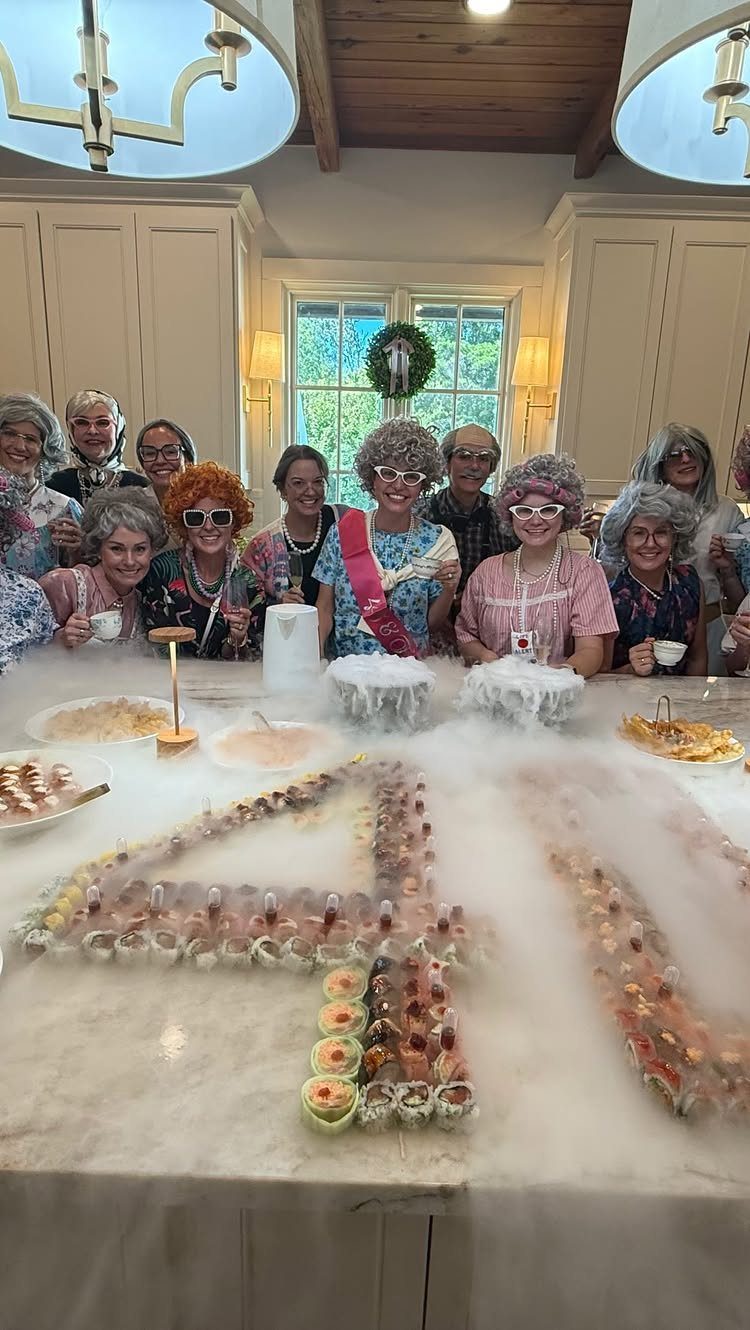 Women in grey wigs posing behind a food display forming the number 40.