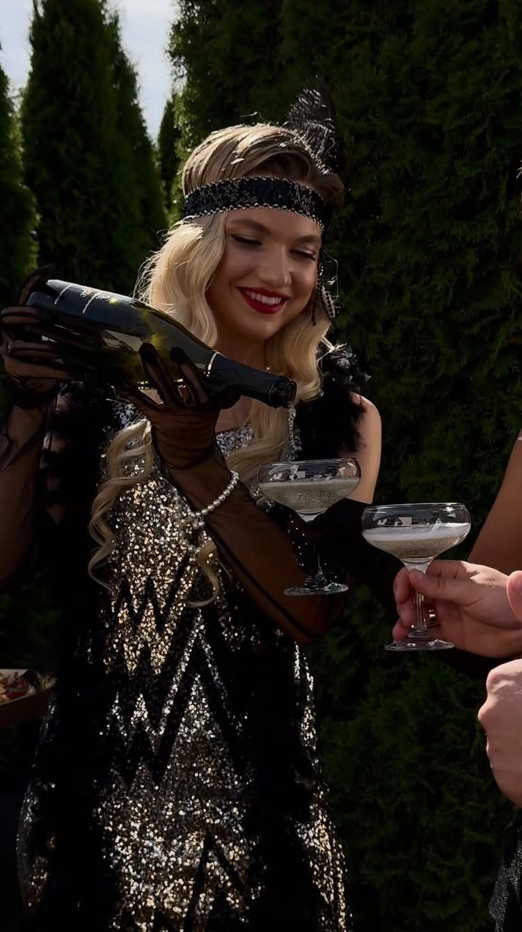 Woman in 1920s flapper dress pouring champagne into glasses at a party.
