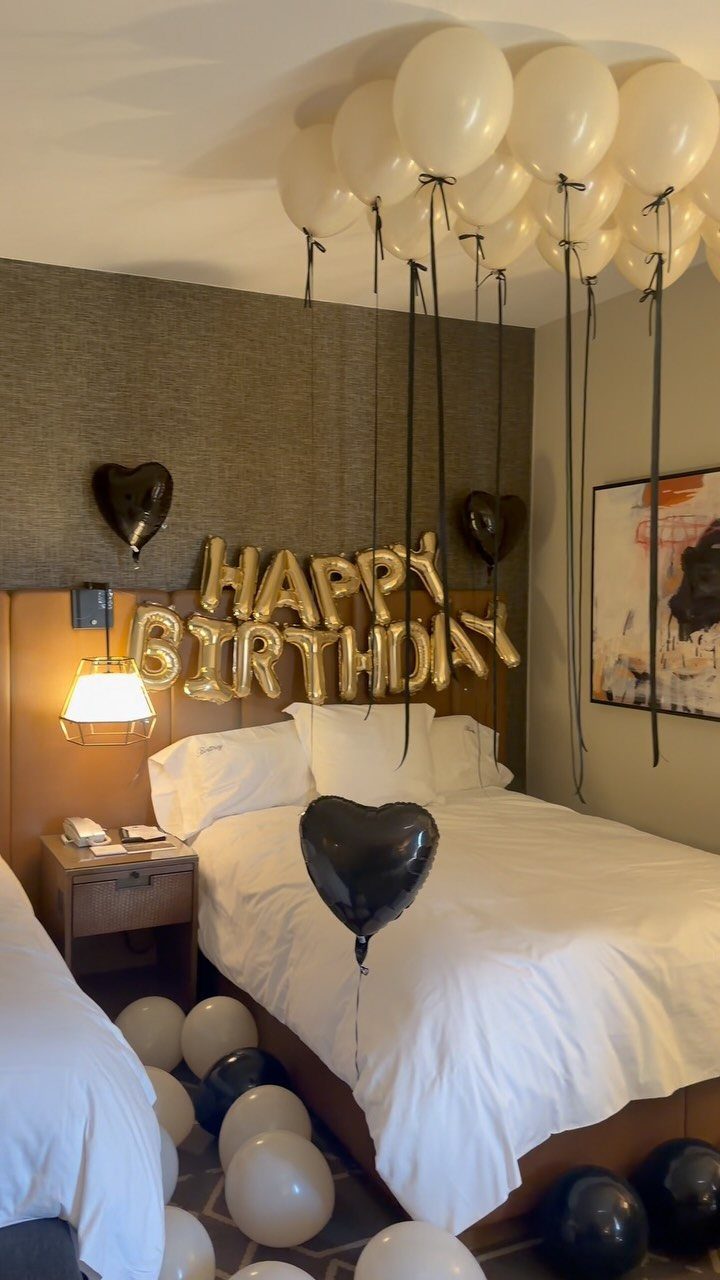 Hotel room decorated with gold birthday balloons, black heart balloons, and white balloons.