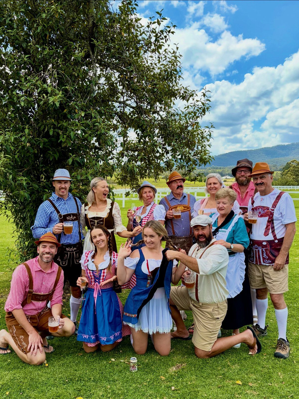 Group of people in traditional Bavarian clothing holding beer glasses in a grassy field.