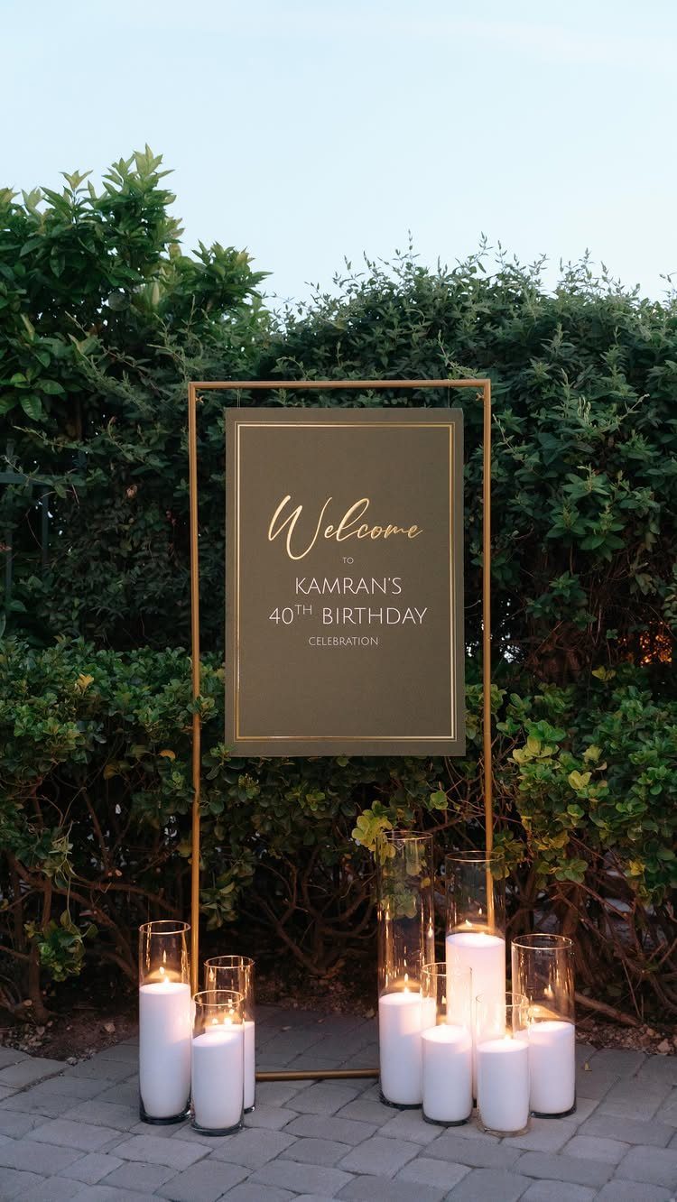 Gold welcome sign for a 40th birthday celebration surrounded by white pillar candles.