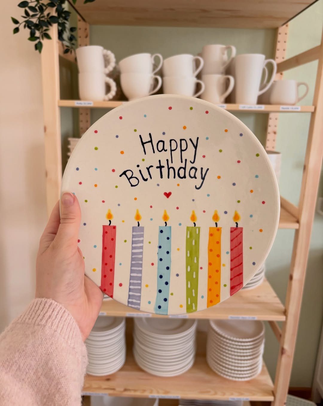 Hand holding a hand-painted ceramic birthday plate with colorful candles in a studio