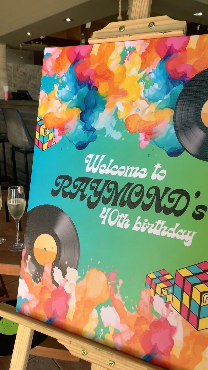Colorful 40th birthday welcome sign with vinyl records and Rubik's cubes on easel