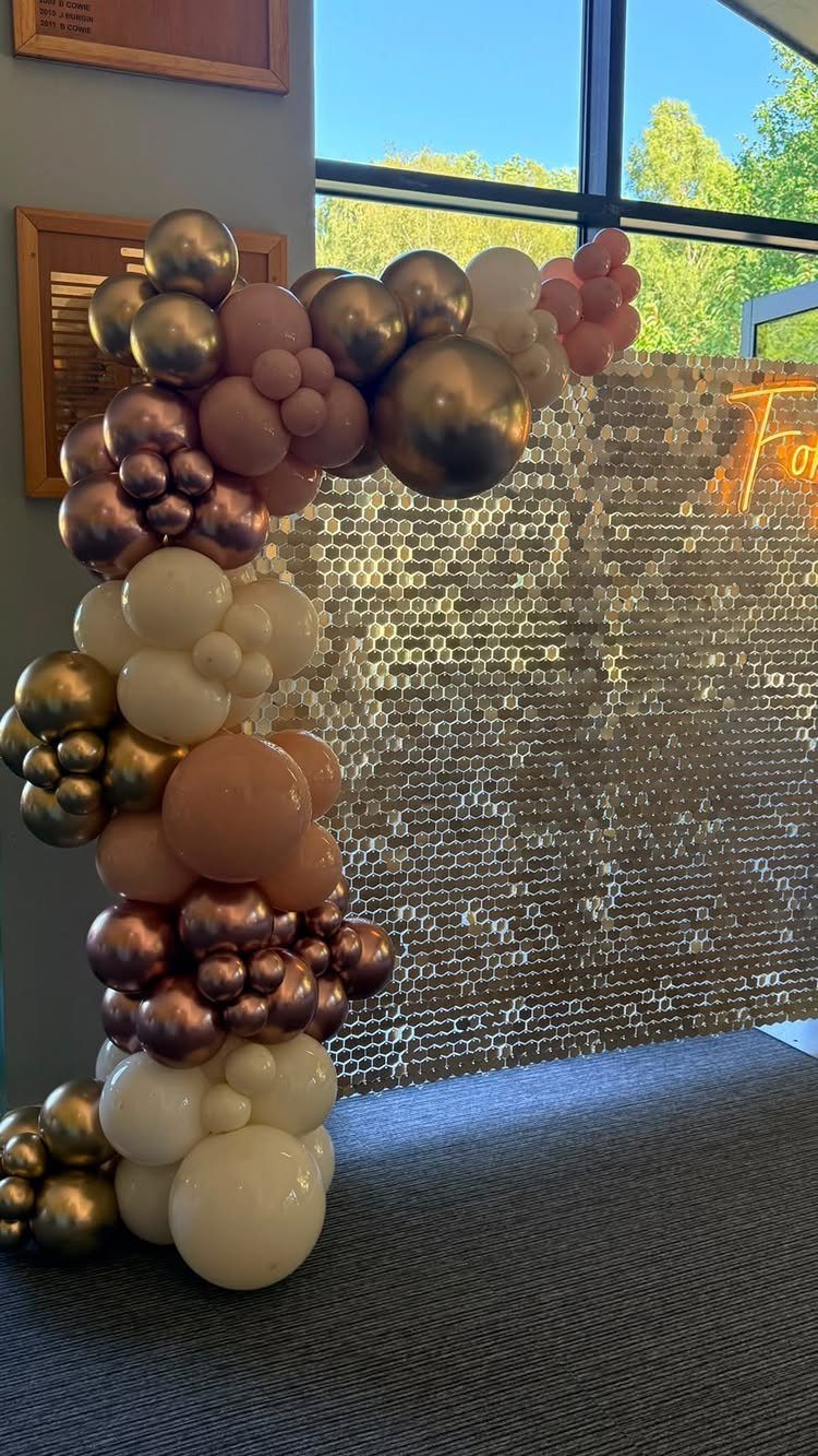 Balloon arch with gold and white balloons beside a gold sequin backdrop wall.