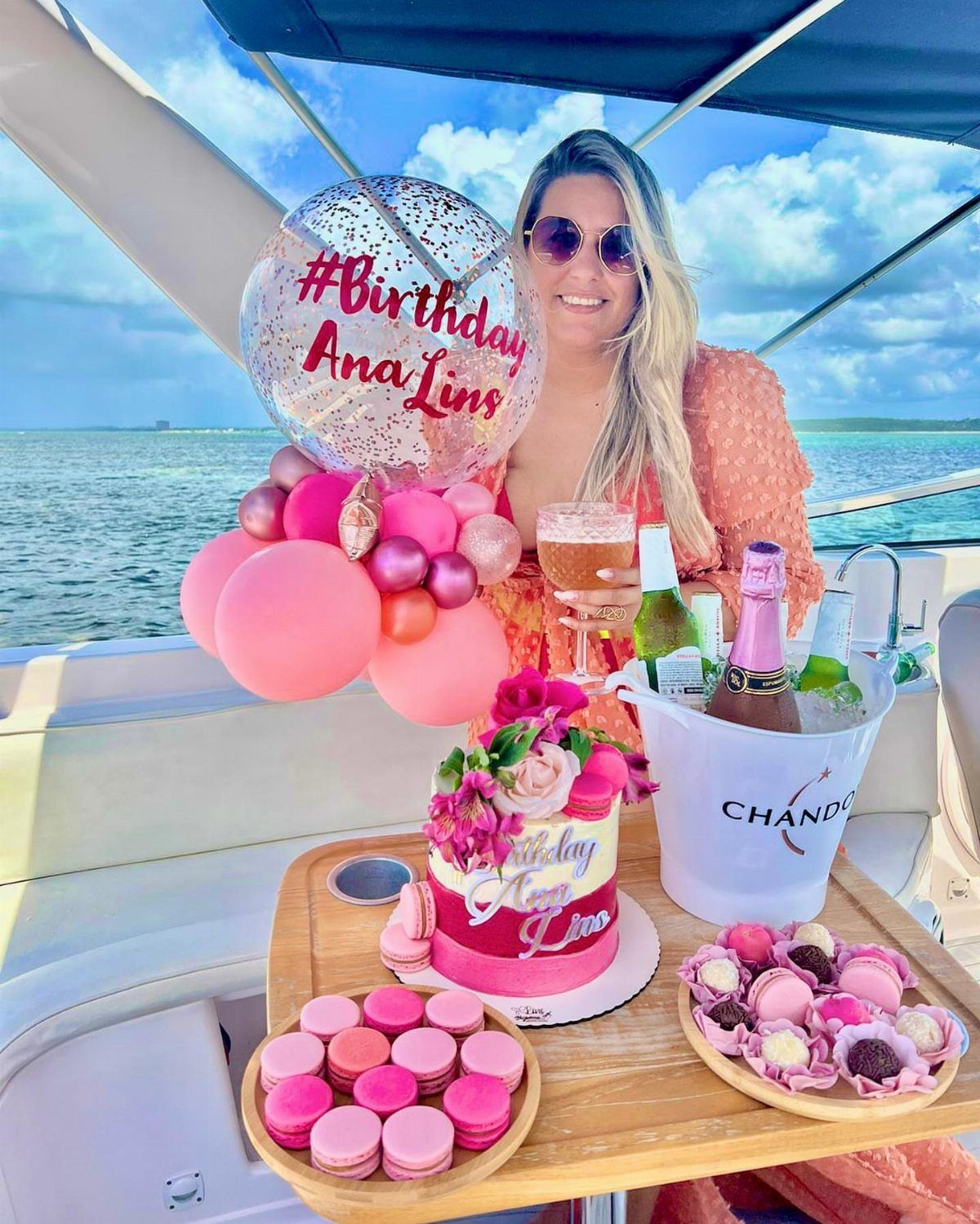 Woman celebrating her birthday on a boat with pink balloons, cake, and champagne.