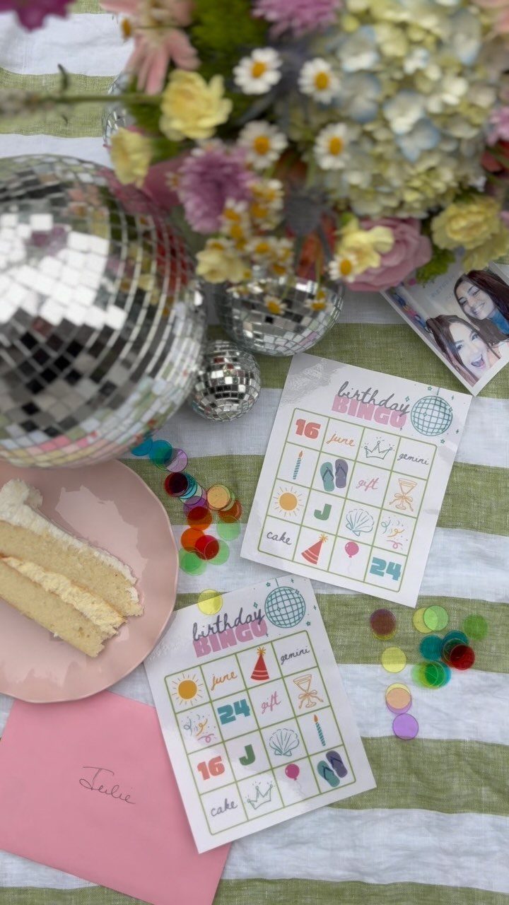 Birthday Bingo cards on a striped tablecloth with a disco ball and flowers.