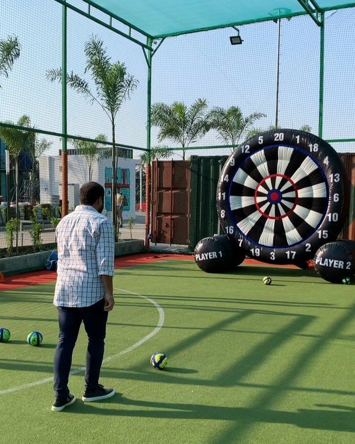 Man standing on green turf facing a giant inflatable dartboard game outdoors.