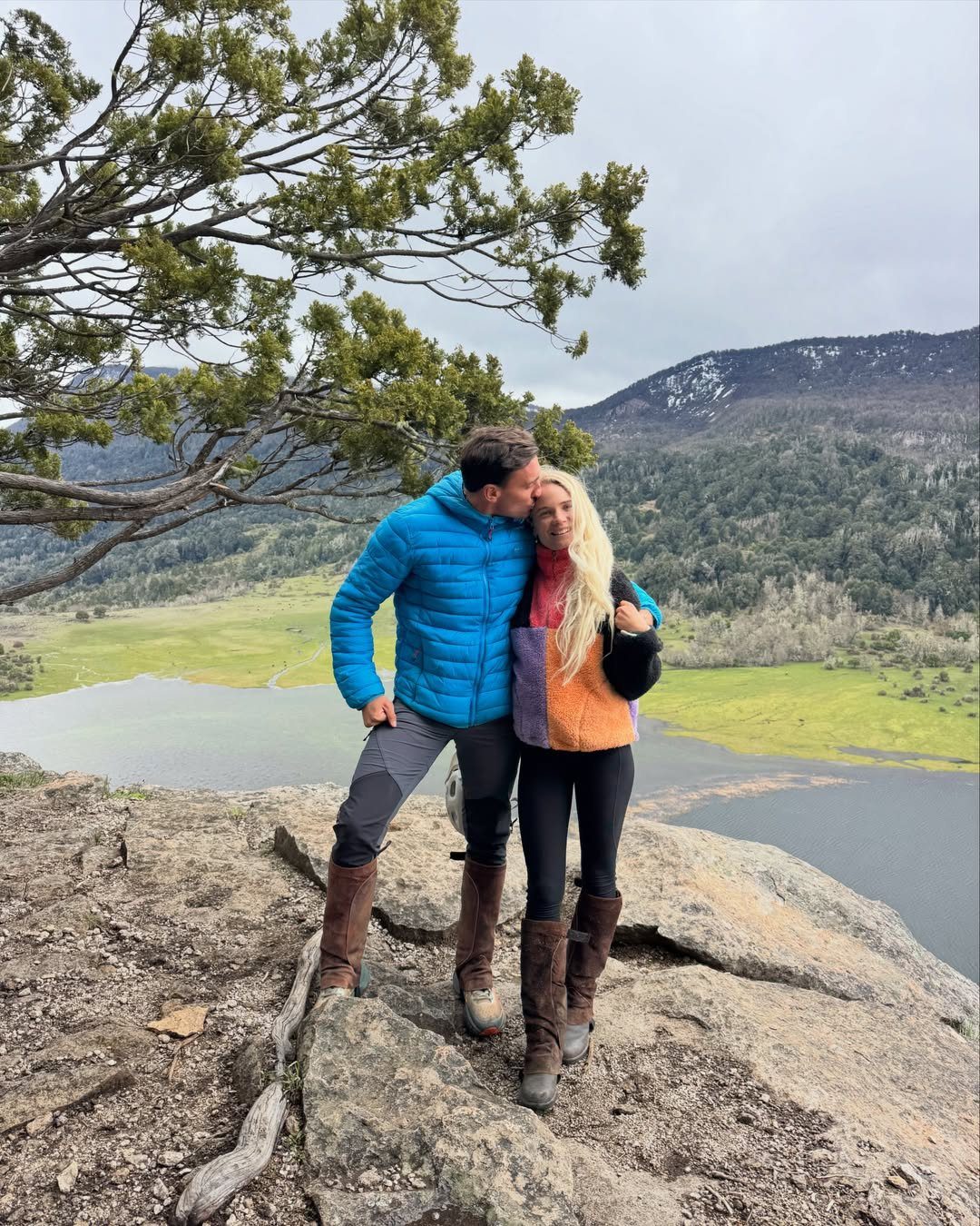 Couple standing on a rocky cliff overlooking a scenic lake and mountain valley.