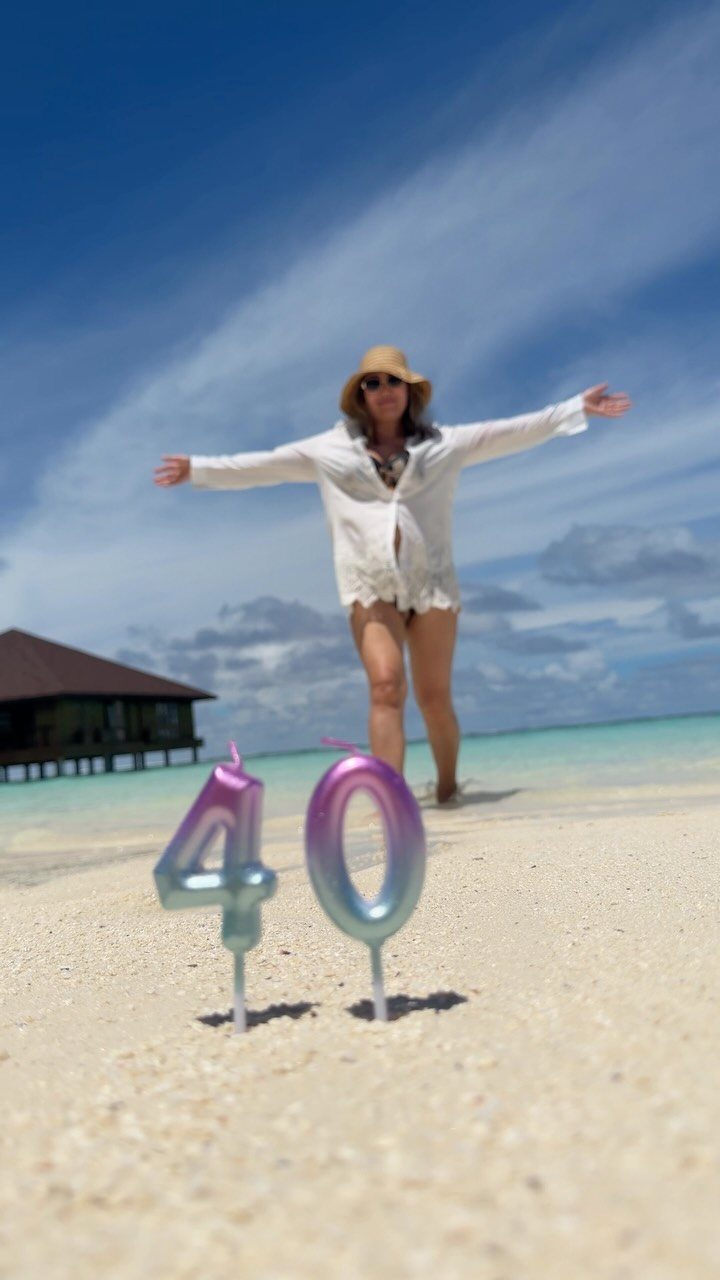 Woman celebrating 40th birthday on a tropical beach with iridescent number candles.