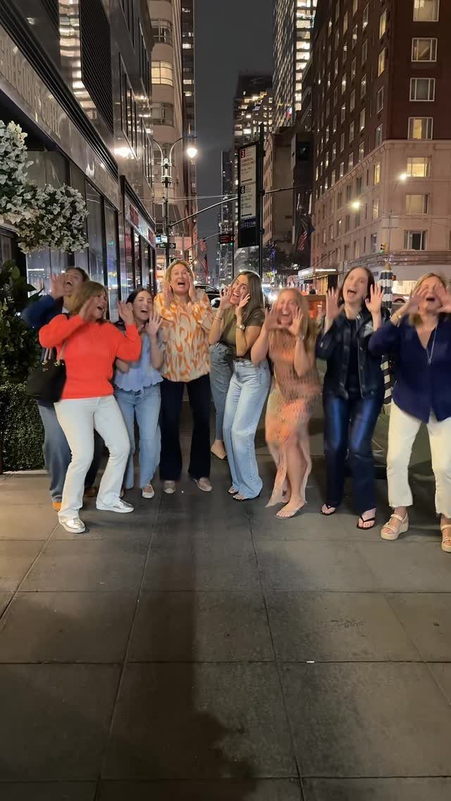 Group of women cheering and posing on a New York City sidewalk at night.