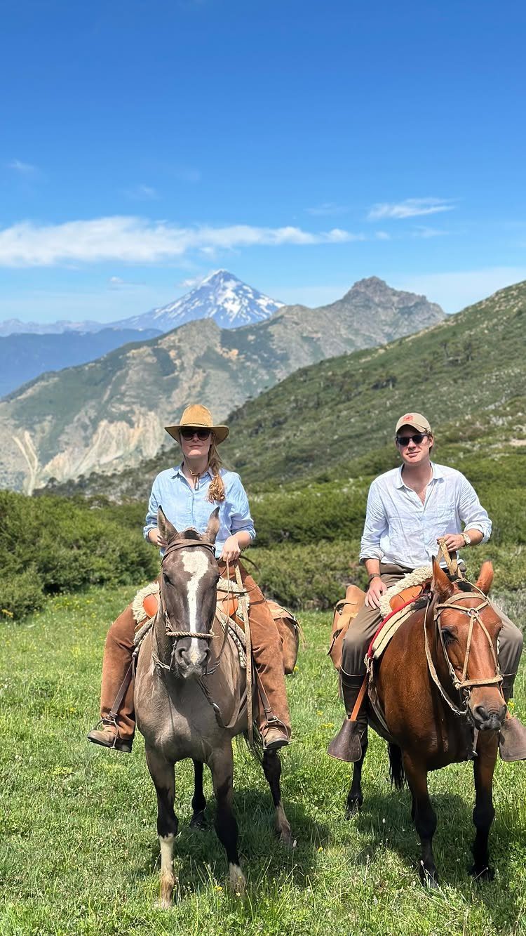 Man and woman on horseback posing in a mountain landscape under blue sky
