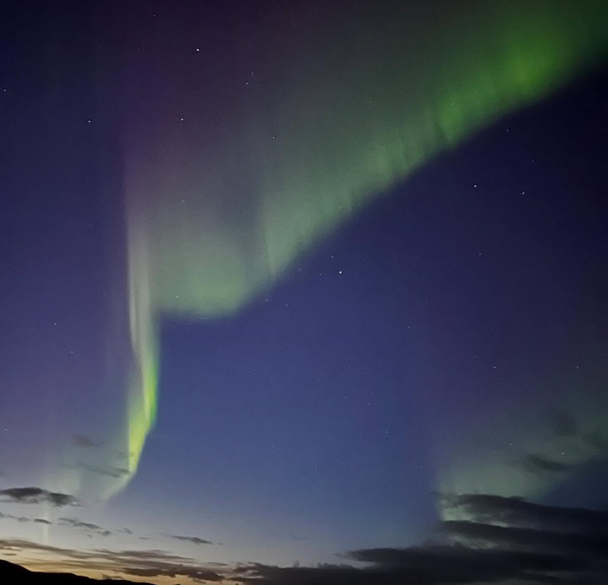 Green aurora borealis dancing across a dark starry night sky over clouds