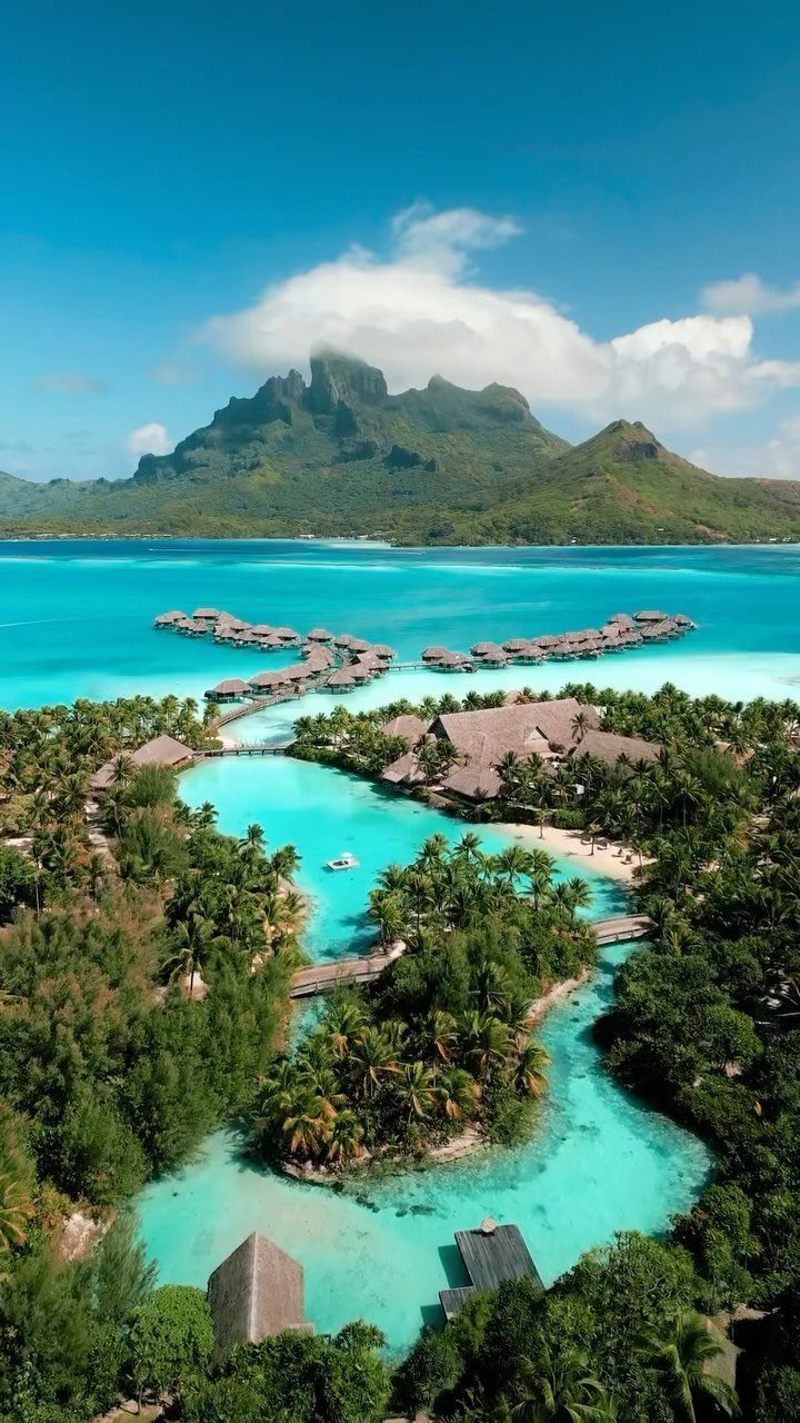 Overwater bungalows in turquoise tropical waters with a mountain in the background.