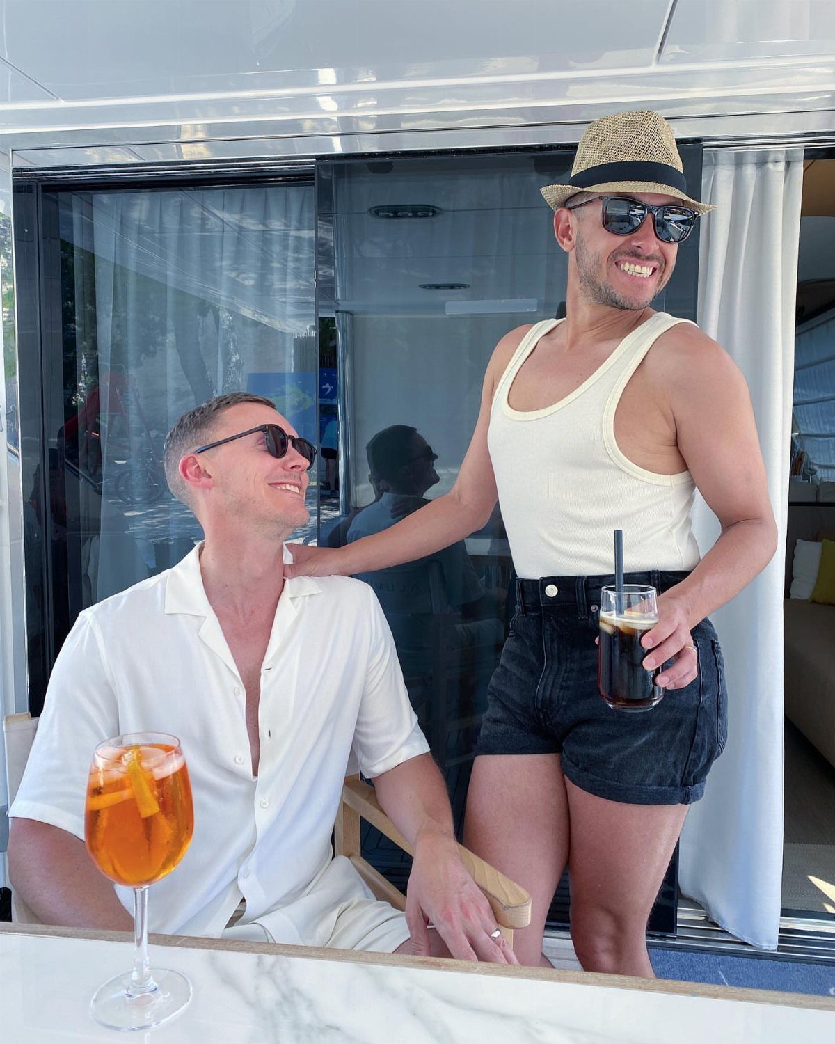 Two men posing on a white boat with cocktails and sunglasses.