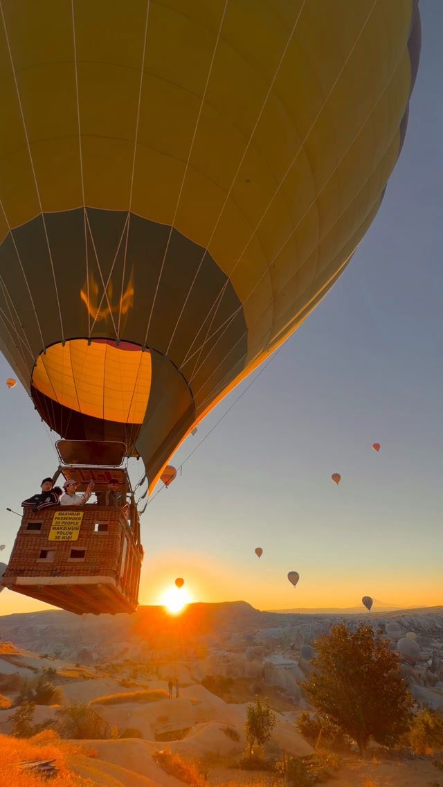 Yellow hot air balloon floating over a rocky valley during a golden sunrise.