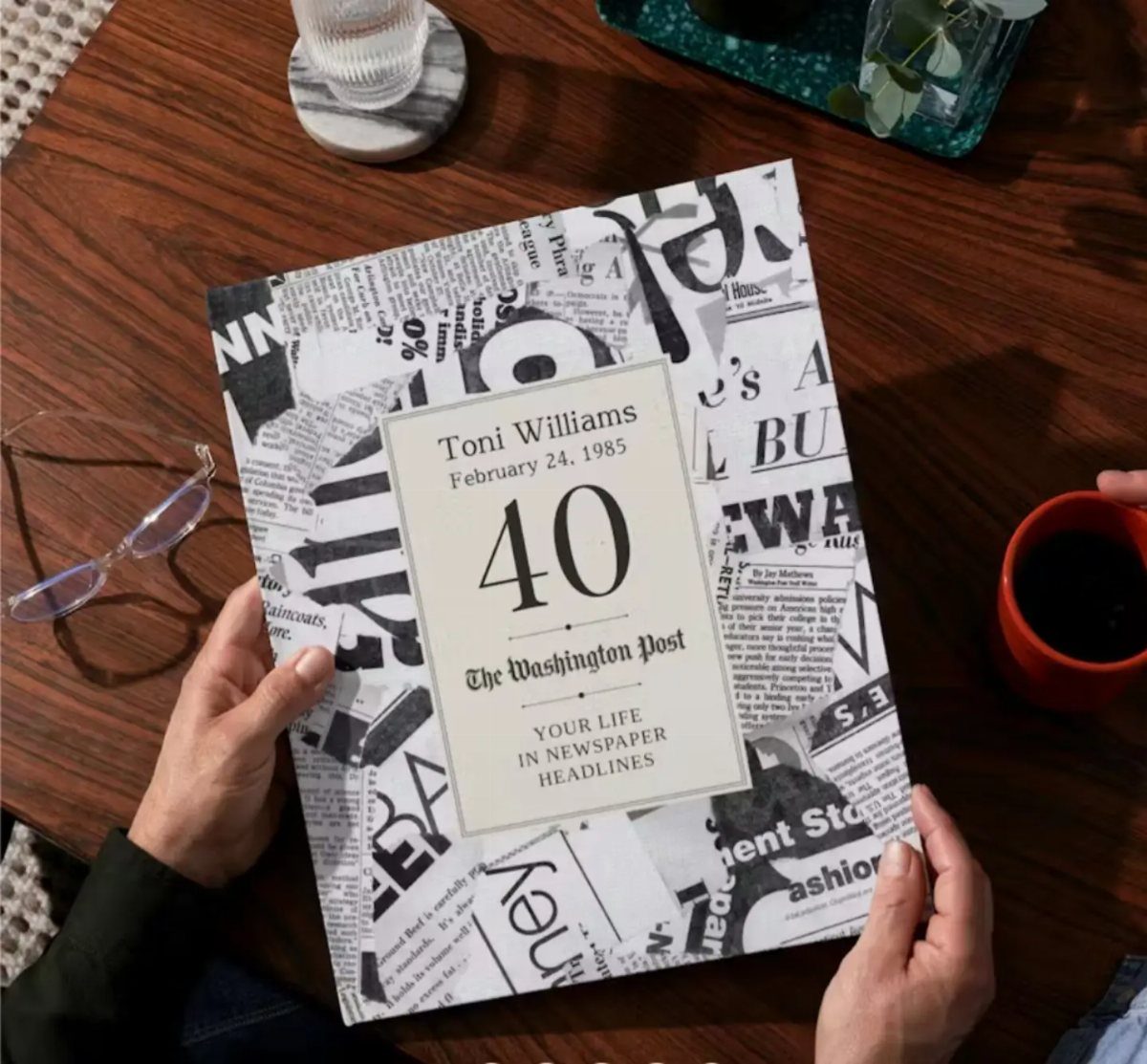 Personalized 40th birthday book with newspaper headlines held over a wooden table.