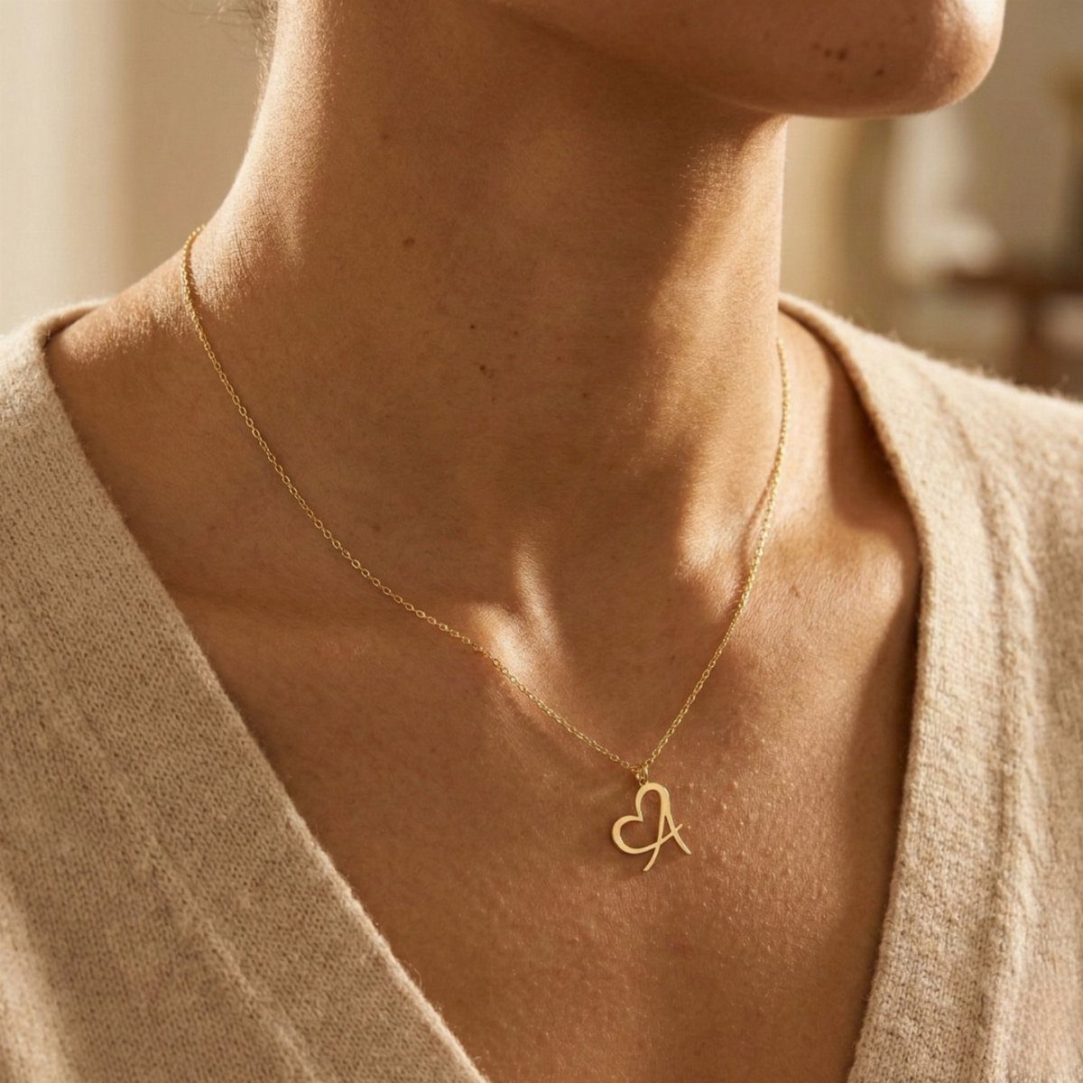 Gold heart necklace with initial A worn by a person in beige clothing