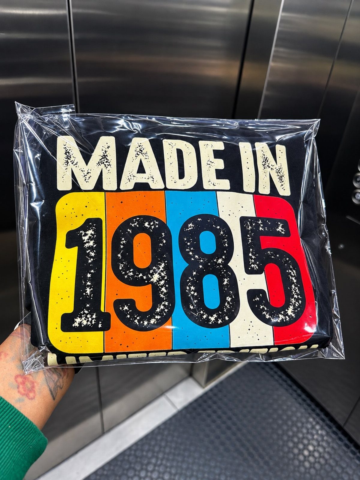Black sweatshirt with Made in 1985 text and colorful stripes in plastic packaging