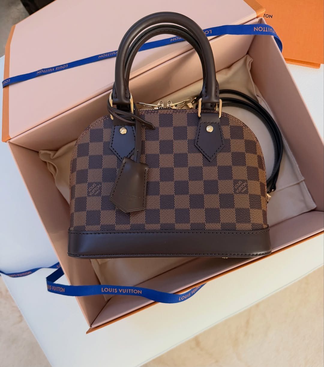 Louis Vuitton checkered handbag inside a branded pink and orange gift box