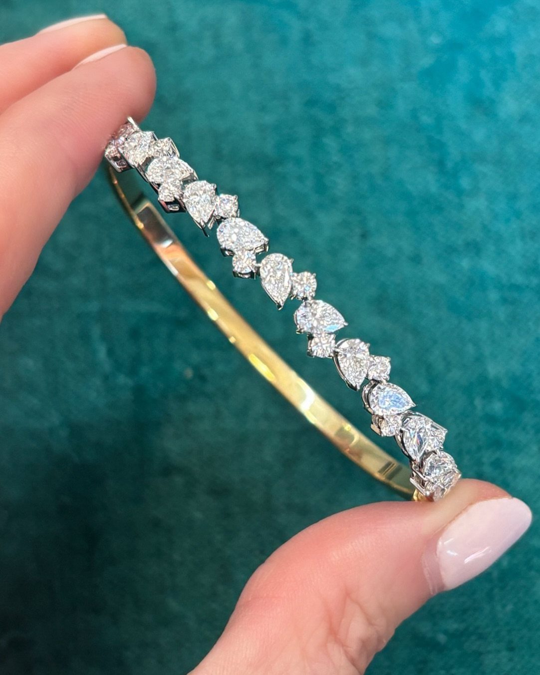 Diamond and gold bangle bracelet held by fingers against a teal background