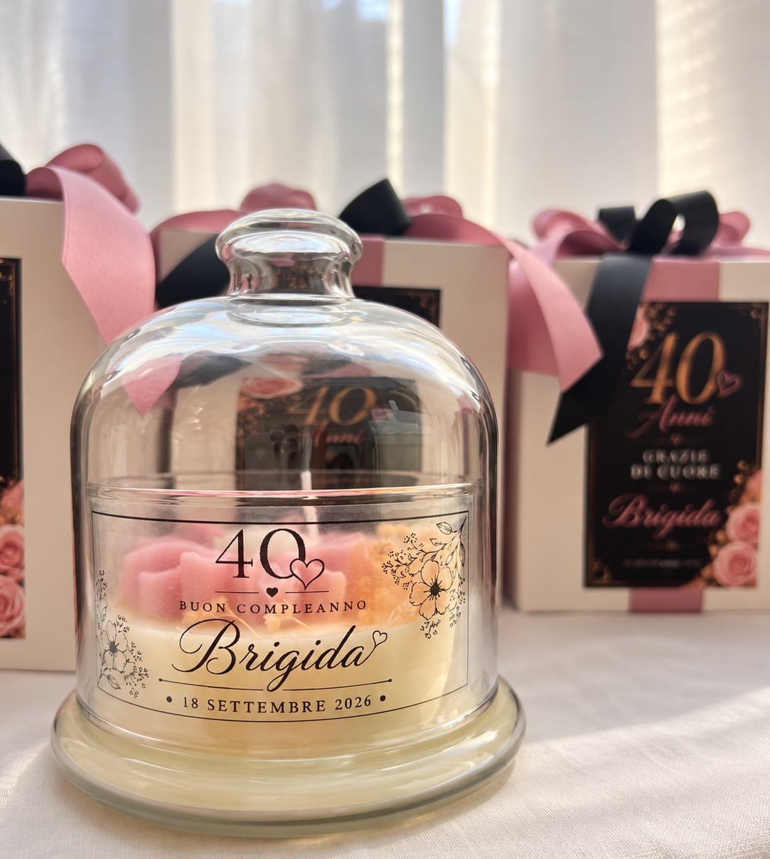 Personalized 40th birthday candle in a glass cloche with gift boxes behind.
