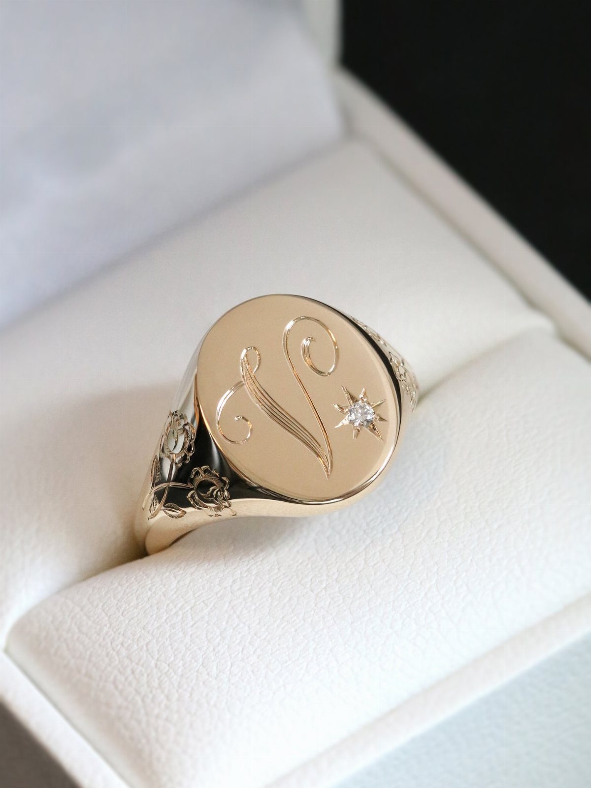 Gold signet ring with engraved letter V and diamond in white box