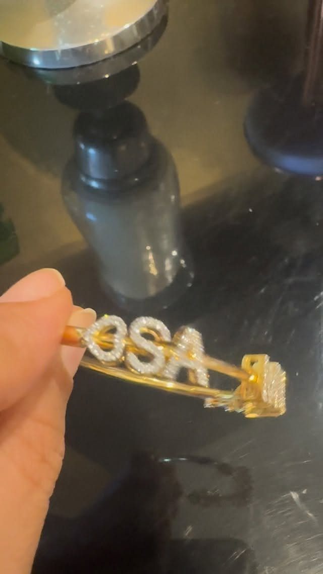 Gold bracelet with crystal letters OSA held by a hand over dark surface