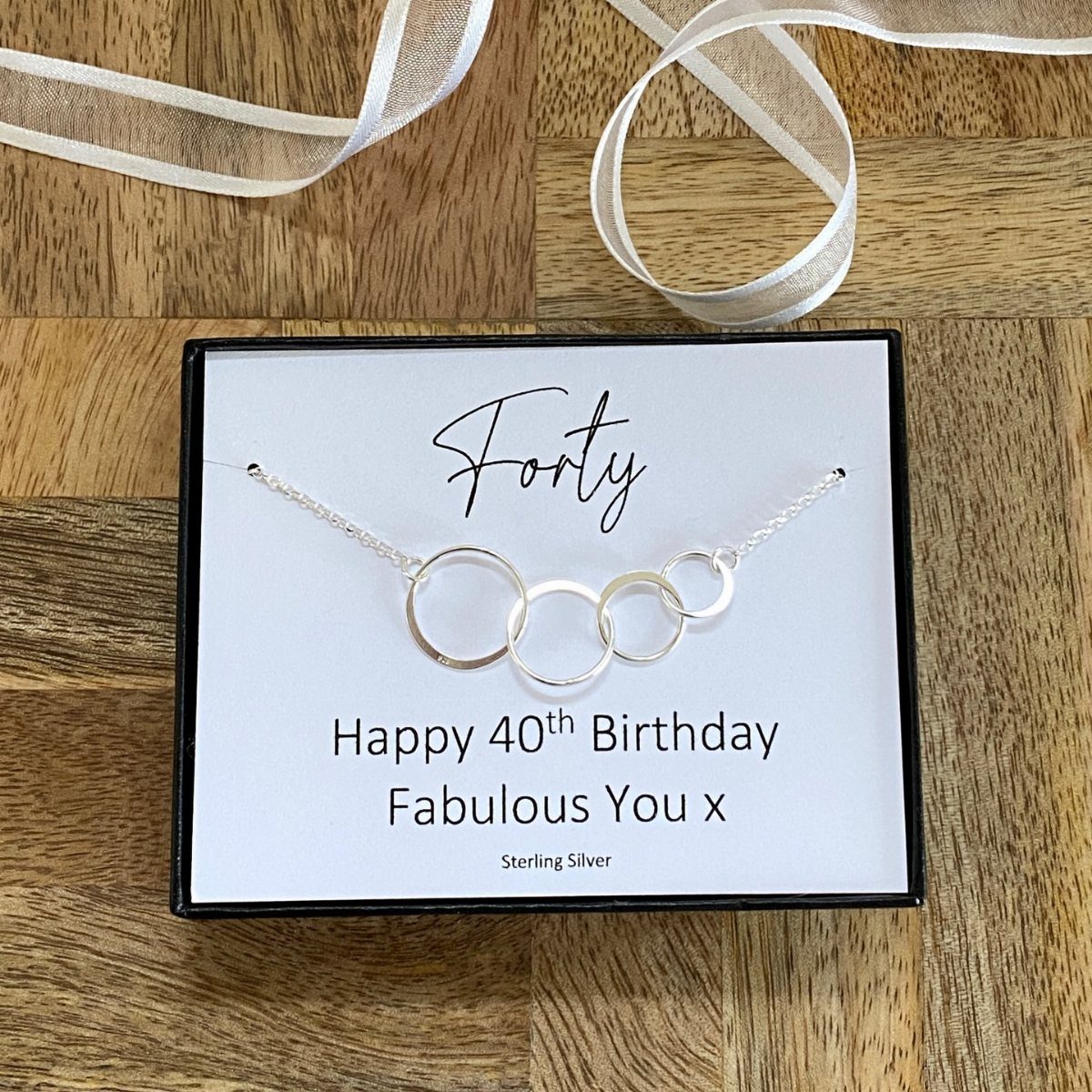Silver interlocking ring necklace in a 40th birthday gift box on wooden background