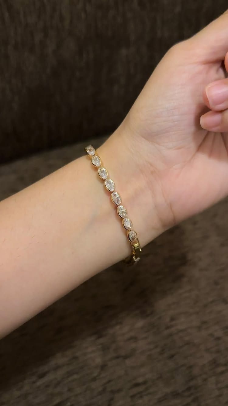 Gold tennis bracelet with oval clear gemstones worn on a person's wrist.