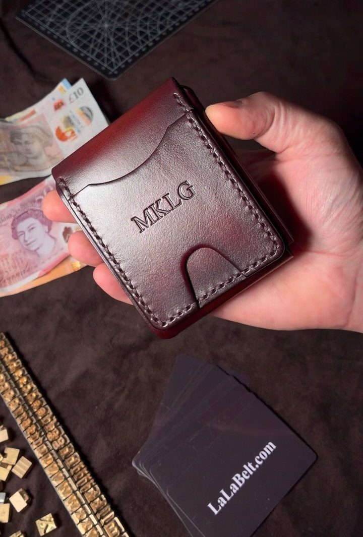 Burgundy leather wallet with embossed initials held in a hand over banknotes.