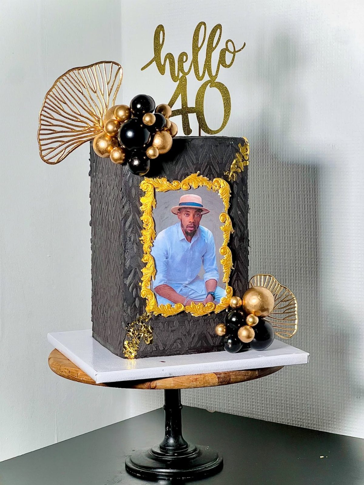Black and gold 40th birthday cake featuring a framed edible portrait of a man.
