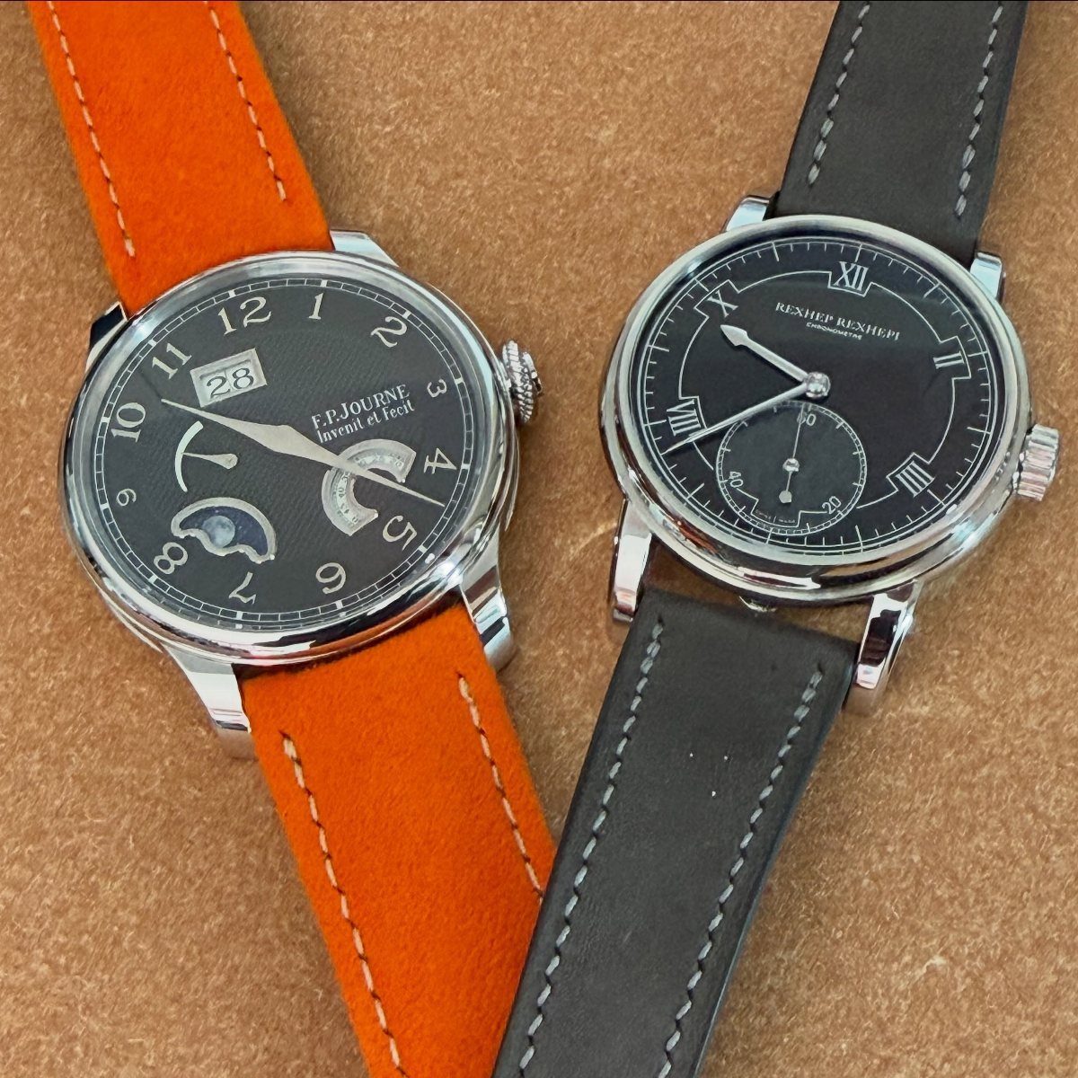 Two luxury wristwatches with orange and grey leather straps on a tan background