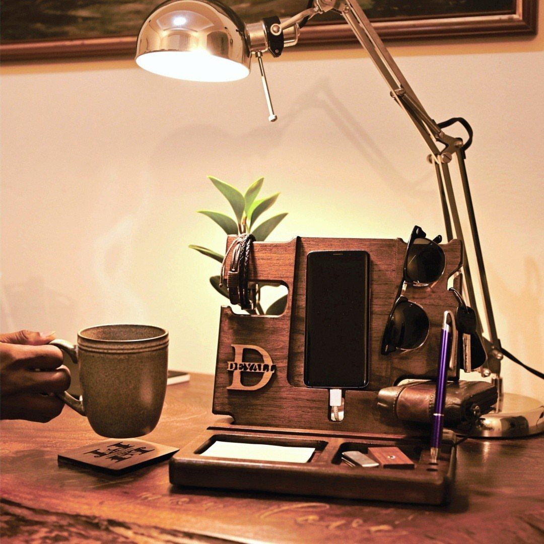 Wooden phone docking station holding a smartphone and sunglasses on a lit desk