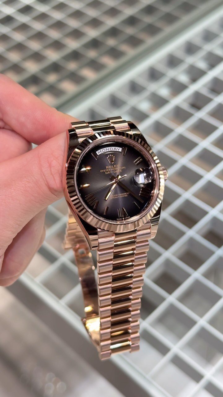 Rose gold luxury wristwatch held by a hand against a white grid background