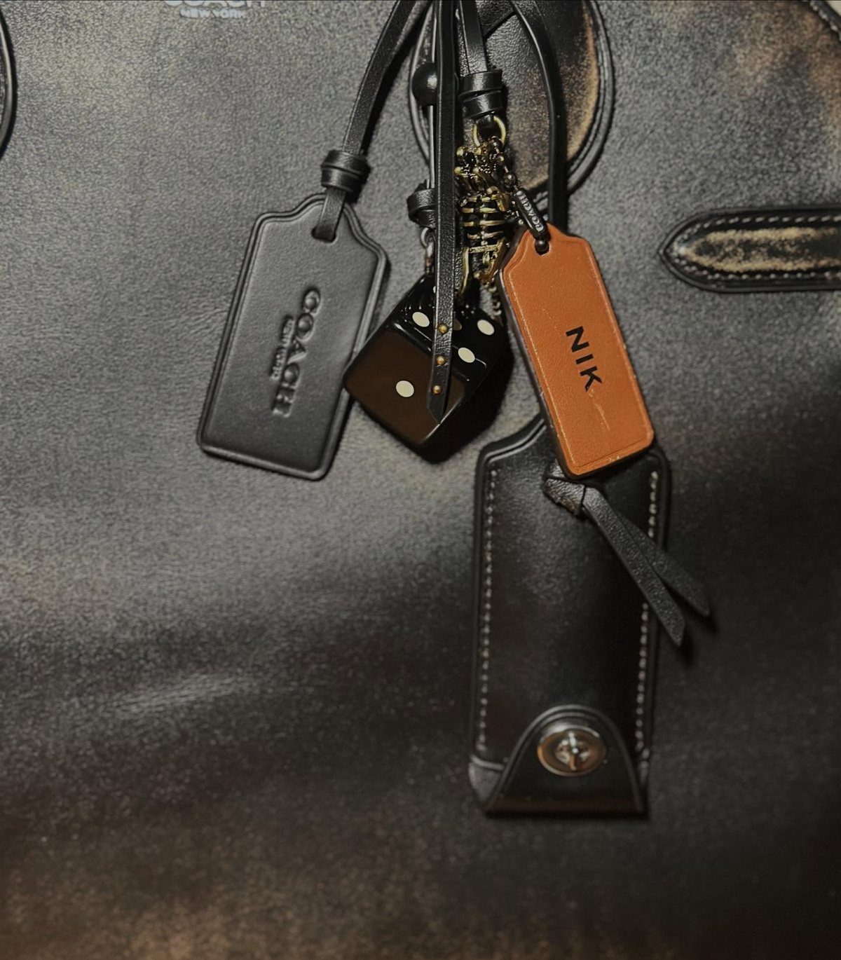 Black leather bag with Coach tag, a die charm, and personalized tan leather tag.