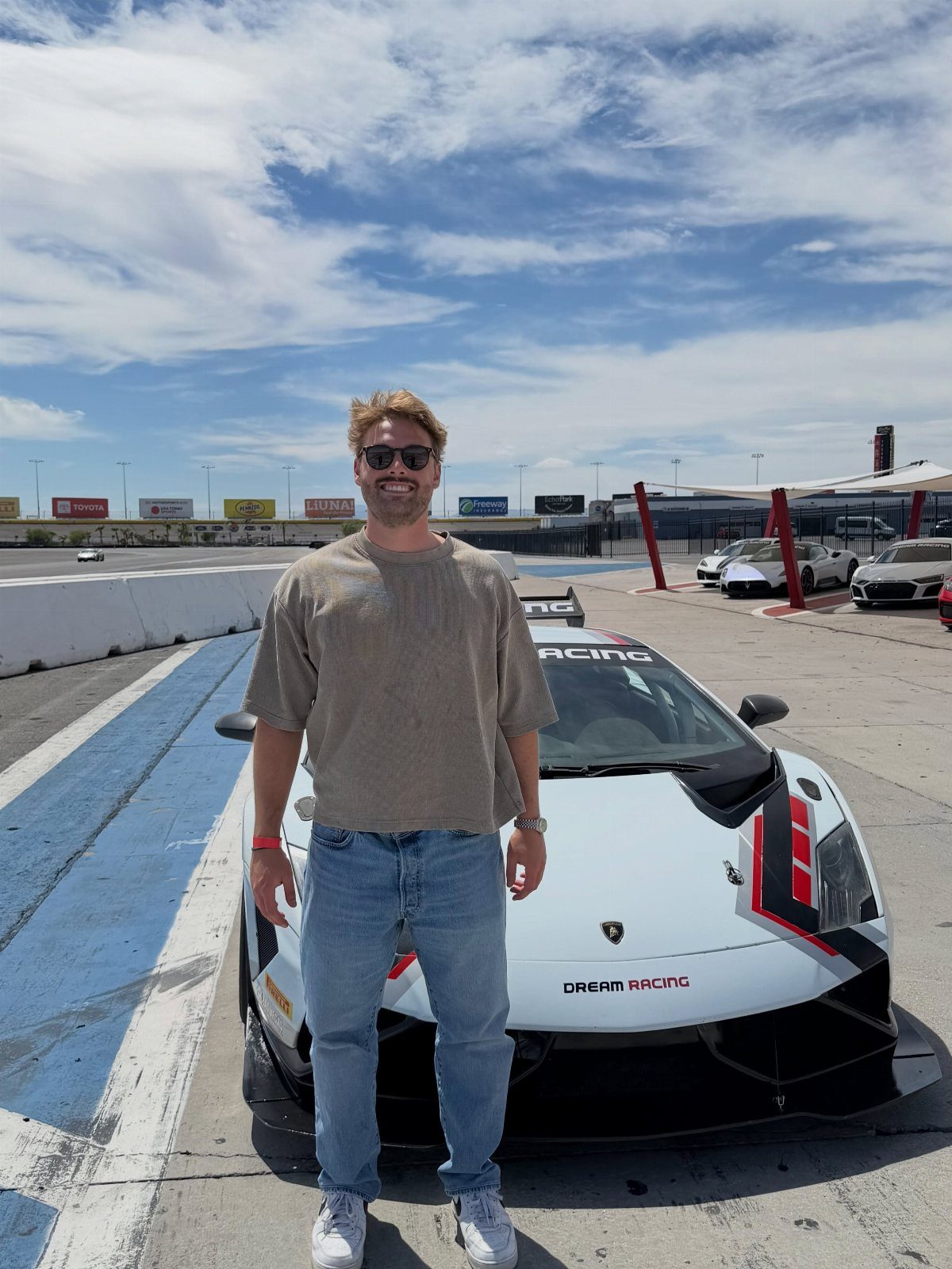 Man standing in front of a white Lamborghini supercar on a racing track.
