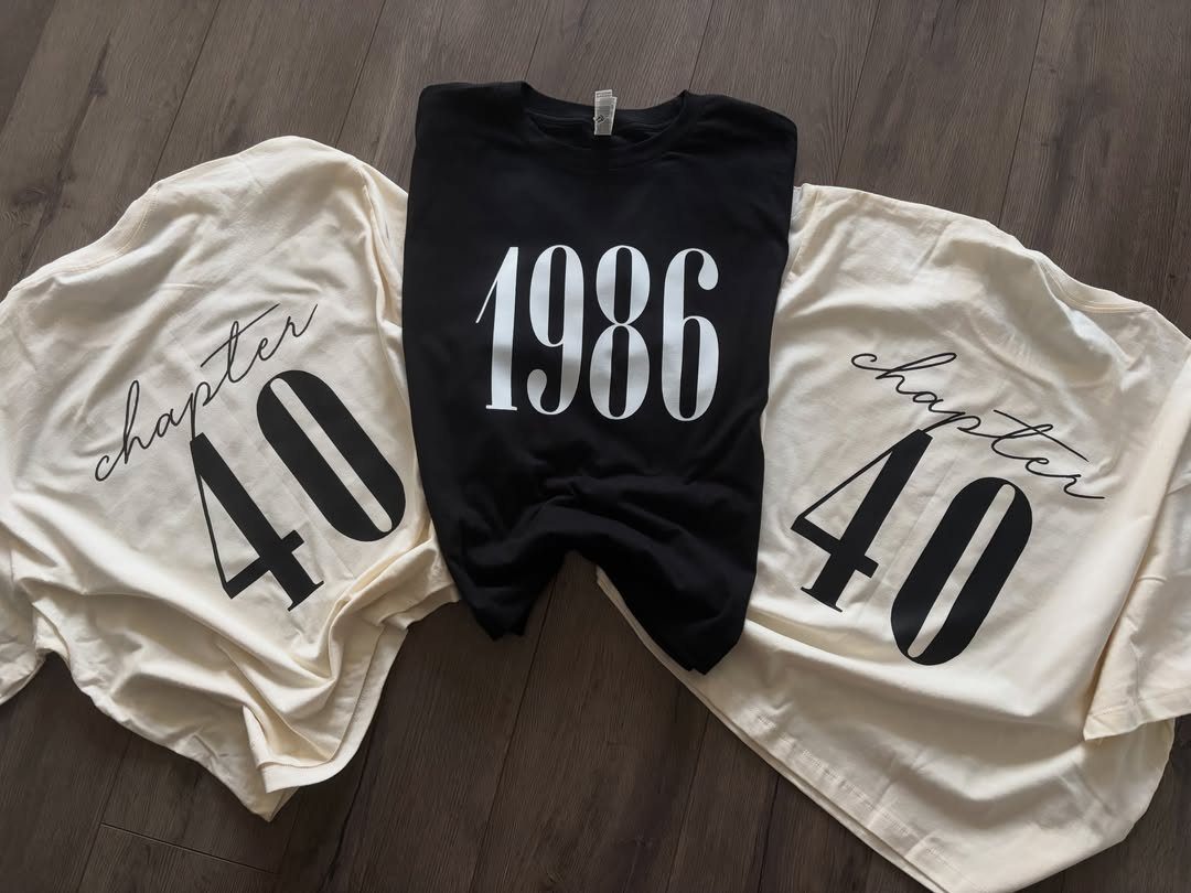Three birthday t-shirts on a wood floor featuring chapter 40 and 1986 prints