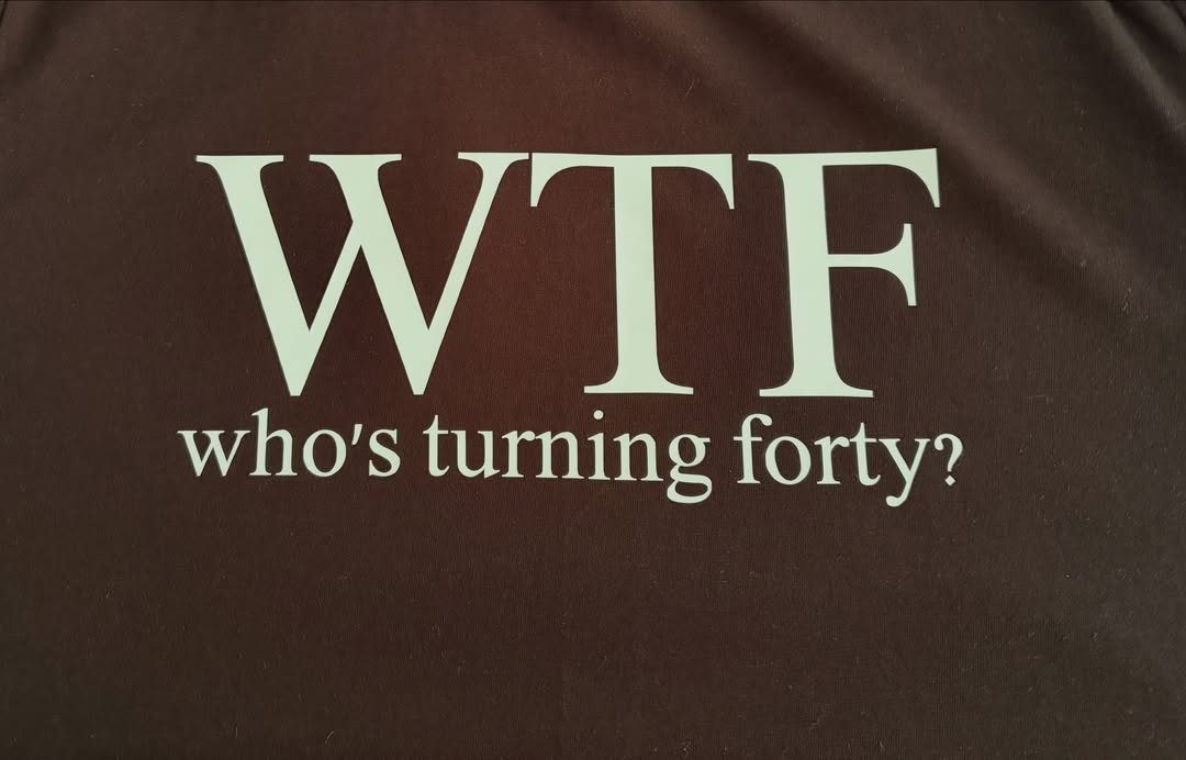 Brown t-shirt with white text reading WTF who's turning forty?